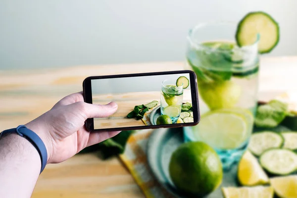 Ve bir akıllı telefon alıp serinletici bir suyun fotoğrafını çekiyor. Salatalık, limon ve iyi bir bitkiyle. Sağlıklı içki ve detoksifikasyon