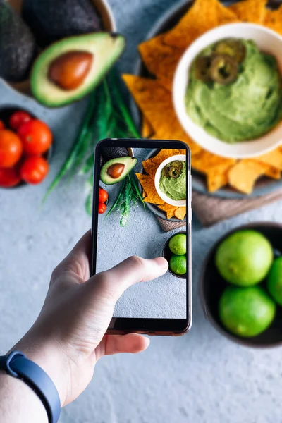 Akıllı telefonu kaldırıp guacamole soslu bir kasenin fotoğrafını çeken eller. Mesaj için yer var. Seçici odak
