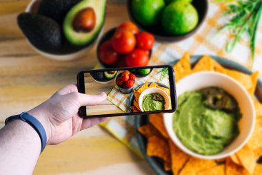 Akıllı telefonu kaldırıp guacamole soslu bir kasenin fotoğrafını çeken eller. Mesaj için yer var. Seçici odak