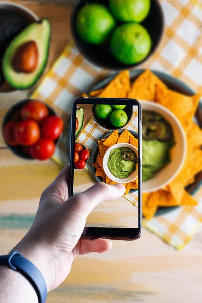 Akıllı telefonu kaldırıp guacamole soslu bir kasenin fotoğrafını çeken eller. Mesaj için yer var. Seçici odak