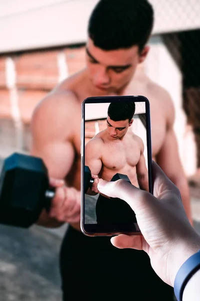 Eller bir akıllı telefonu kaldırır ve dışarıda egzersiz yapan genç bir adamın fotoğrafını çeker. Mesaj için yer var. Seçici odak