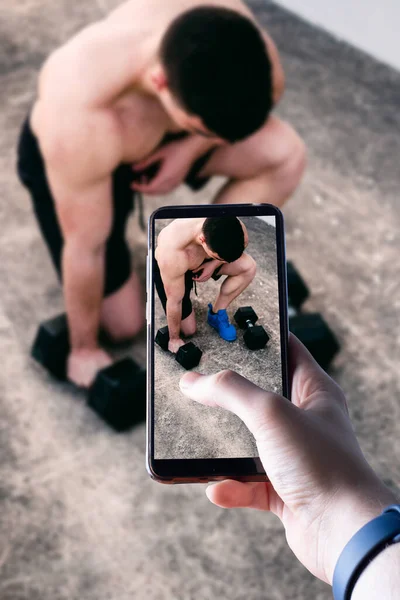 Eller bir akıllı telefonu kaldırır ve dışarıda egzersiz yapan genç bir adamın fotoğrafını çeker. Mesaj için yer var. Seçici odak