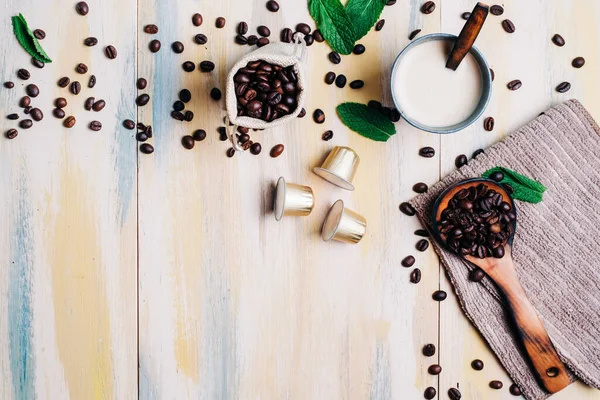 Kahve çekirdekleri, hafif ahşap masa, kahve kapsülü ve bir fincan kahve. Üst Manzara. Kopyalama alanı.