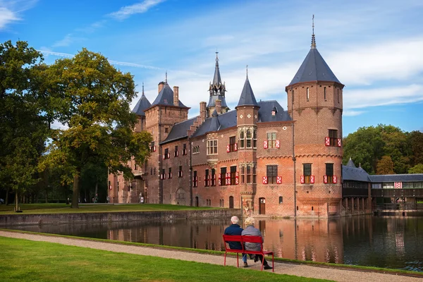 Bejaarde echtpaar zittend op een bankje voor het middeleeuwse kasteel De Haar in de buurt van Utrecht, Nederland — Stockfoto