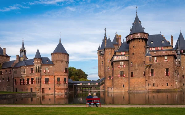 Pareja mayor sentada por la noche en un banco rojo frente al castillo medieval De Haar, cerca de Utrecht, Países Bajos — Foto de Stock