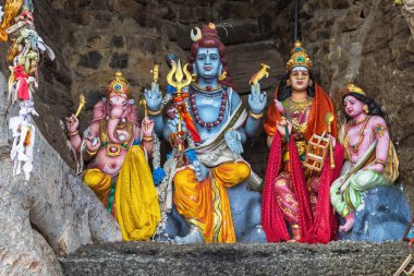 Trincomalee / Sri Lanka - 18 Kasım 2019: Ağaçların kökleri arasındaki mağarada Hindu tanrılarının renkli figürleri 