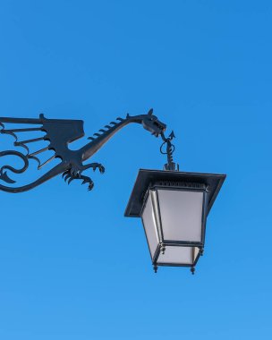 Efsanevi bir ejderha şeklinde metal bir tepeye asılmış sokak lambası.