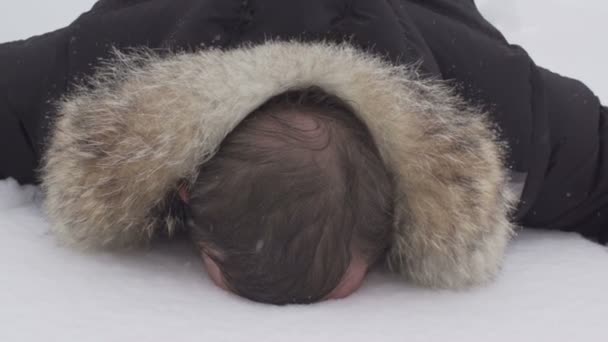 Egy férfi fekszik a hóban, arccal lefelé, lassított felvétel — Stock videók
