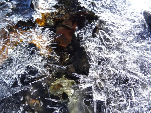 山の川の太陽の氷のパターンで救済の輝きの水と茶色の石を介して — ストック写真