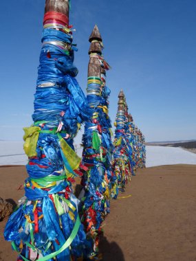 Mavi gökyüzü, kar ve kumdan oluşan arka planda çok renkli kurdelelerle bağlanmış ayin sütunlarının dikey fotoğrafı
