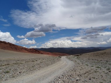 Moğol dağlarındaki yol manzarası güzel turuncu yamaçlardan geçip mavi gökyüzü ve alçak beyaz bulutların altındaki vadiye iniyor.