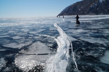 Baykal Gölü 'nün koyu mavi buzunda yürüyen bir grup turist.