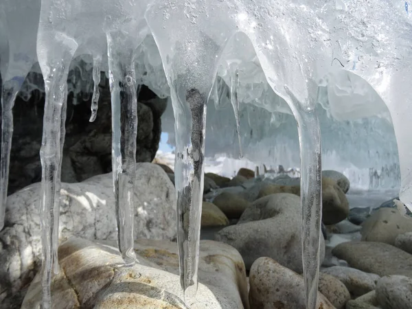 an ice cap with icicles hangs over the round stones, and a piece of blue sky is visible through it