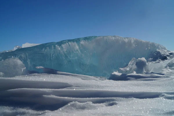 青い空に太陽の光の下で輝く雪の上に氷の大きな透明なブロックが横たわっています — ストック写真