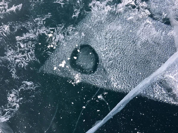濃い青の透明な氷の上に白い気泡と大きな魚のような雪の霧雨のパターン — ストック写真