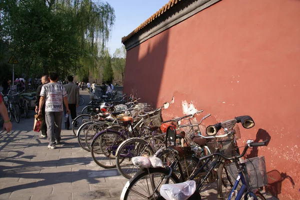 people walk along the sidewalk near the bike Park near the old, terracotta wall. on one of the bikes, gloves are attached to the handlebars.