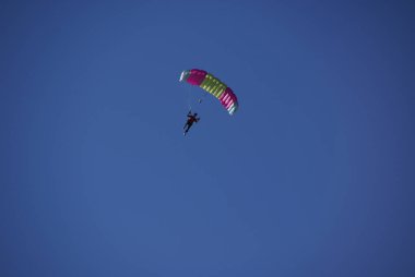 Kırmızı ve sarı kanatlı bir paraşütçü zengin mavi gökyüzünde süzülür..
