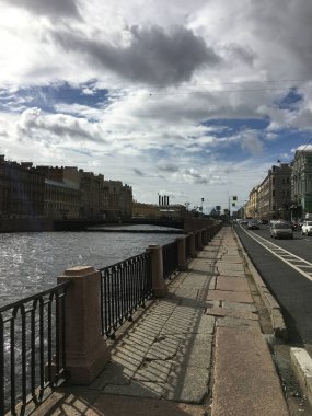 Mavi gökyüzü ve şehrin üzerindeki beyaz bulutlar, kanalın ışıl ışıl suyu, kanal boyunca uzanan yaya yolu.