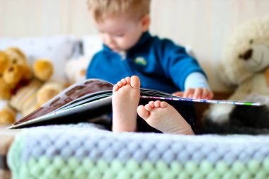 Küçük çocuk, ekose örgü üzerinde oyuncak ayılarla kitap okuyor.