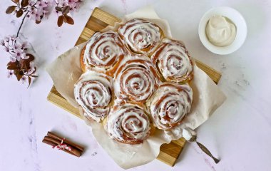 Tarçınlı ve kremalı tarçınlı çörekler, beyaz arkaplandaki tahta dallarda çiçek açan dallar.