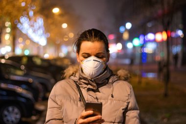 Onu virüslerden, dumandan, egzoz dumanından ve yoğun sisteki diğer atmosferik kirleticilerden korumak için maske takan genç bir kadın. Sağlık, ekoloji ve hava kirliliği hakkında kavramsal fotoğraf.