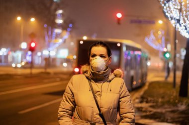Onu virüslerden, dumandan, egzoz dumanından ve yoğun sisteki diğer atmosferik kirleticilerden korumak için maske takan genç bir kadın. Sağlık, ekoloji ve hava kirliliği hakkında kavramsal fotoğraf.
