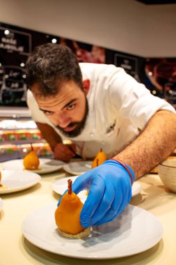 Koruyucu eldiven takan mutfak şefi portakal şarabında kaynatılmış armutla süsleme yapıyor ve mascarpone ceviz kreması ile dolduruluyor. Lezzetli restoran tatlıları. Yemek ve güzel yemek konsepti.