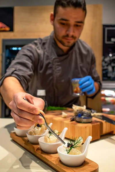  Genç şef bir parça safranı cımbızla aperatiflerin üzerine koyuyor. Eğlence marketi. Restoranlar ve güzel yemek konsepti..
