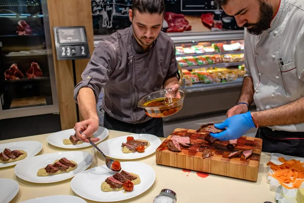Aşçılar, konuklara ikram etmeden önce kuru pirzola bifteği püre ve vişneli domatesle hazırlıyorlar. Mutfakta takım çalışması. Seçici odaklanma. Restoran ve güzel yemek konsepti.