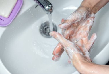  Banyoda musluğun altında ellerini sabunla yıkayan bir kadın. Kapsamlı tıbbi prosedür için adım adım resim talimatları. Altıncı adım, parmaklarınızın arasını yıkayın (içeride).