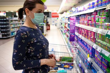 Koronavirüs salgını ve kilit altında tutulma sırasında tek kullanımlık koruyucu maske takan bir kadın süpermarkette alışveriş yapıyor. Covid-19 salgını sırasında Coronavirus salgını önleme tedbirleri.