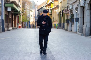  Kilitleme sırasında boş şehir sokaklarında cep telefonuna bakarken şık genç bir adam tek başına yürüyor. Sosyal uzaklık ve yalnızlık kavramı.