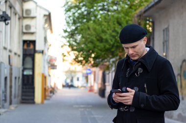 Yalnız genç adam boş bir meydanda tek başına duruyor, mesaj atıyor ya da randevu bekliyor. Yalnızlık kavramı.
