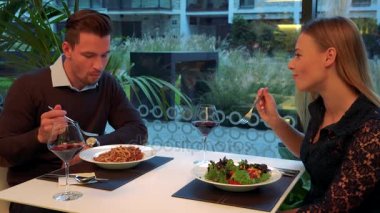Bir erkek ve bir kadın (genç ve çekici) bir restoranda bir masada oturup, yemek, şarap içmek ve konuşmak