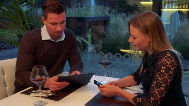 Bir adam ve bir kadın (genç ve çekici) sit bir restoranda bir masada, o bir tablet tutar, o bir akıllı telefon tutar, o bir şey hakkında belgili tanımlık aygıt açıklar