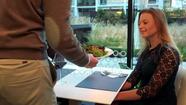 Un camarero trae comida a un hombre y una mujer (jóvenes y atractivos) sentados en una mesa — Vídeos de Stock