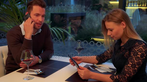 Muž a žena (mladá a atraktivní) sedět u stolu v restauraci, mluví na smartphone, pracuje na tabletu