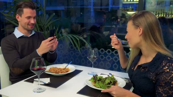 Um homem bonito tira uma foto de uma mulher bonita em uma mesa em um restaurante — Vídeo de Stock