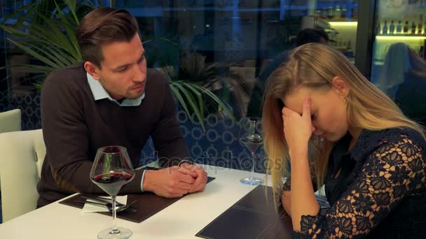 Um homem e uma mulher (jovens e atraentes) sentam-se em uma mesa em um restaurante, a mulher está triste, o homem tenta confortá-la — Vídeo de Stock
