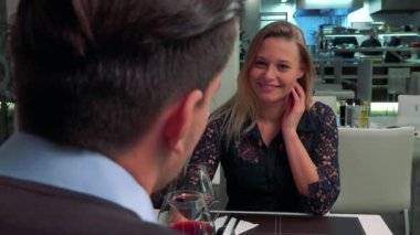 Genç, güzel bir kadın ve bir erkek (başının arkasına kameraya) bir restoranda bir masada oturup, şarap içmek ve konuşmak