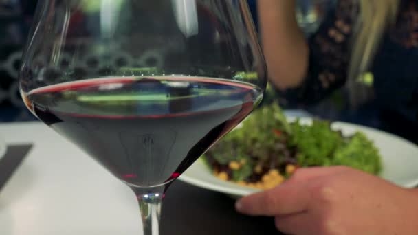 Um copo de vinho - close-up, uma mulher come salada no fundo embaçado — Vídeo de Stock