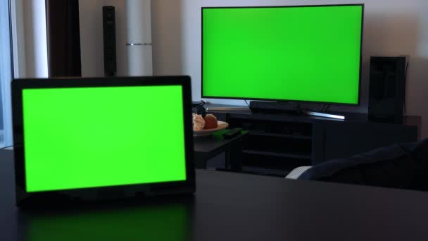 A tablet on a desk in a horizontal position - a TV in the background, both have green screens — Stock Video