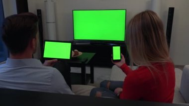 Bir erkek ve bir kadın kanepede oturup, o bir tablet tutar, o bir akıllı telefon, bir Tv içinde belgili tanımlık geçmiş - tüm üç yeşil ekran tutar