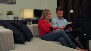 Çekici bir genç çift bir kanepede o bir akıllı telefon tutar ve ona o tutar tablet hakkında açıklar