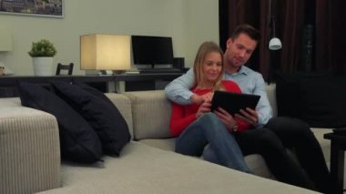 Bir genç, çekici çift rahat bir oturma odasında bir kanepede oturuyor, kadın bir tablet tutar ve bir şey için adamı tarif etmeye yeterli