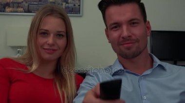 Çekici bir genç çift kamera önünde adam kamera - closeup arkasında bir TV kanalları geçer
