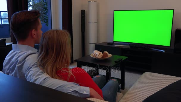 Una joven pareja ve un televisor con pantalla verde en una acogedora sala de estar — Vídeos de Stock