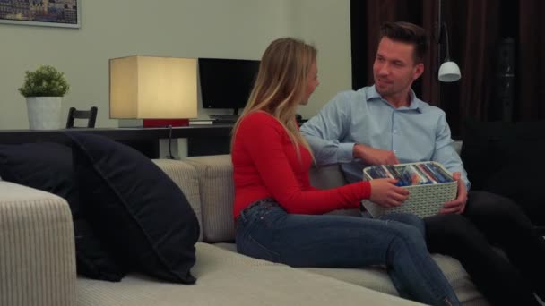 Un hombre y una mujer (jóvenes y atractivos) se sientan en un sofá, el hombre muestra sus DVDs — Vídeo de stock
