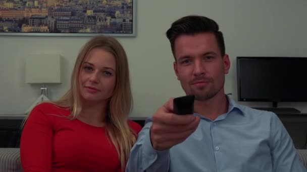 Egy férfi és egy nő (fiatal és vonzó) nézz a kamerába, majd az ember rákattint egy Tv távirányító - Vértes — Stock videók