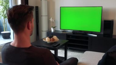 Bir adam rahat bir oturma odasında yeşil bir ekran bir Tv izliyor